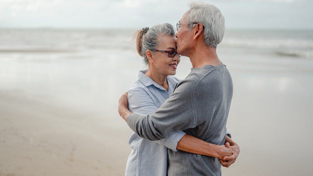 Senior couple hug and kiss each on the beach. Plan life insurance with a happy retirement concept.