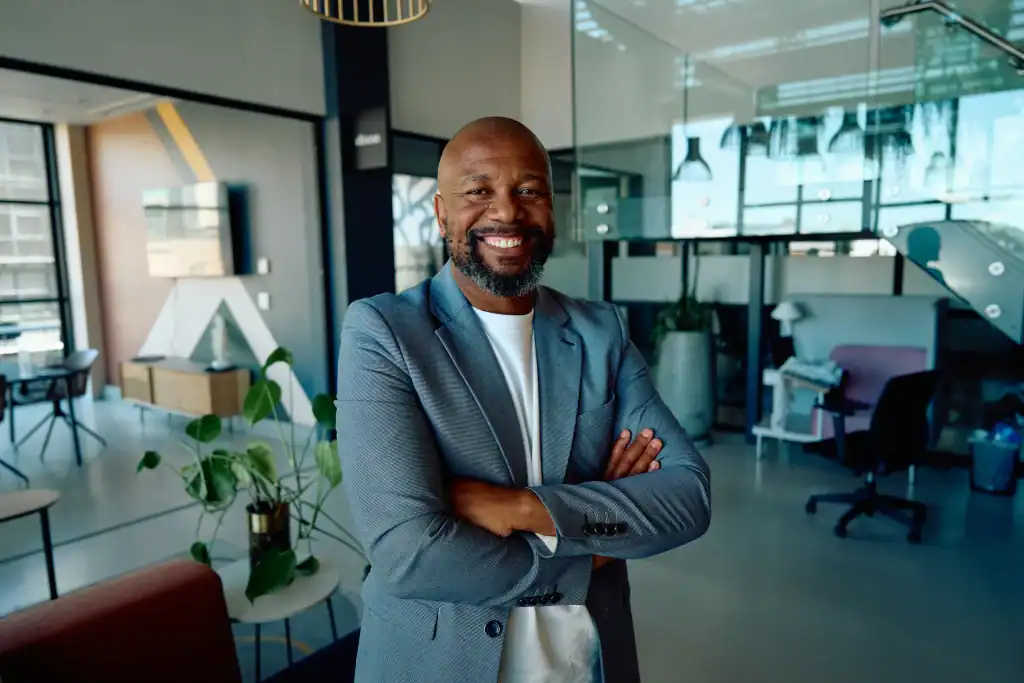 Portrait of smiling black mature businessman in blazer standing arms crossed in modern office